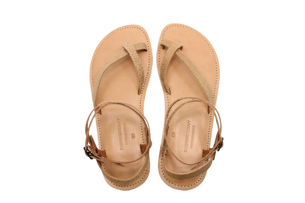 Une paire de sandales en cuir beige, dotées de lanières entre les orteils et de brides à la cheville, présentées côte à côte sur un fond blanc.