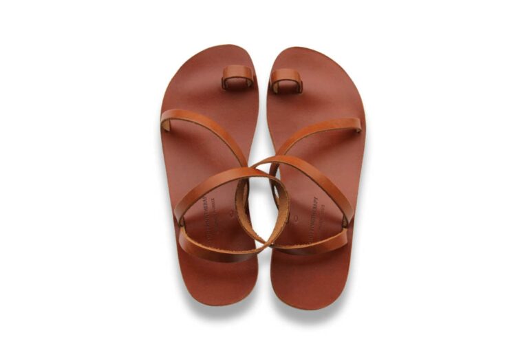 A pair of brown leather sandals with minimalist straps and a toe loop, placed side by side on a white background.