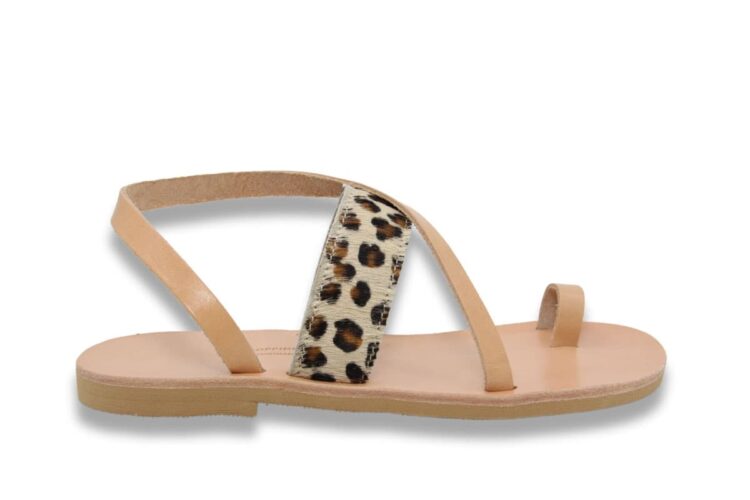 Sandale en cuir naturel vachetta beige avec une bride sur le coup de pied à imprimé léopard, une boucle d'orteil et une bride diagonal sur le coup de pied et qui passe derrière la cheville, affichée sur un fond blanc. Vue latérale. Modèle Patmos Leo.